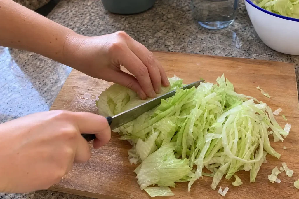 Ett par händer strimlar isbergssallad på skärbräda, en påminnelse om att goda sallader som står för sig själva börjar med ...