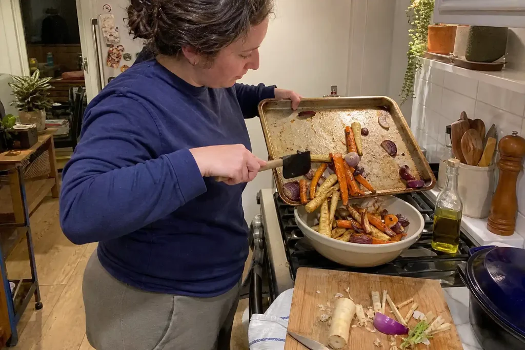 En person häller nyrostade rotsaker från plåten i en skål vid spisen, ett exempel på Goda sallader som står för sig själva.