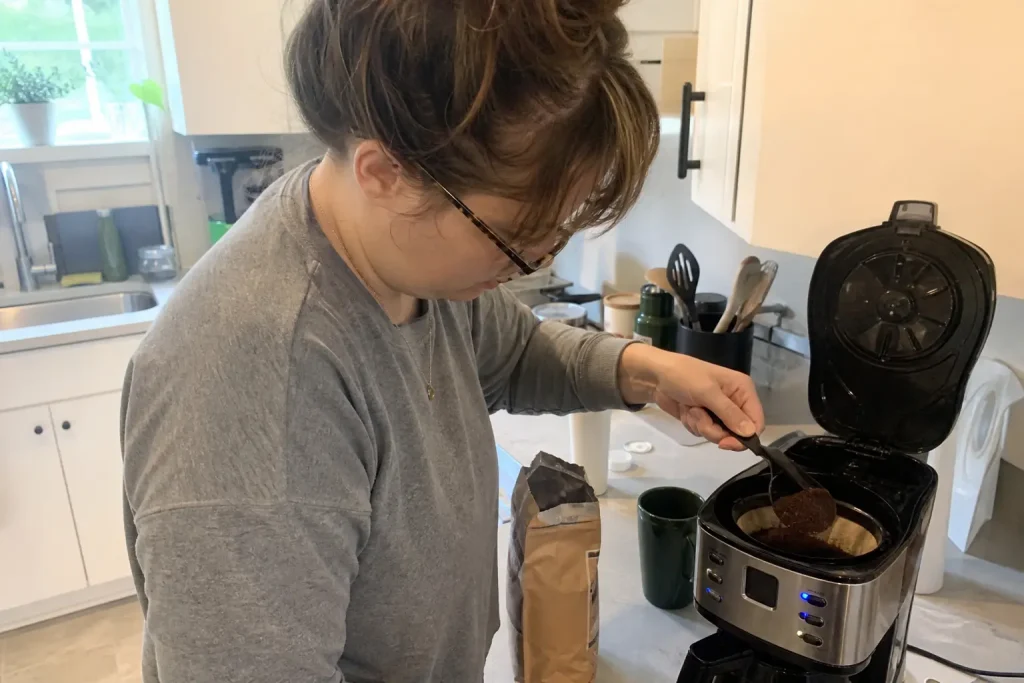 Person skopar kaffe i bryggare vid köksbänken en vardagsmorgon, ett exempel på kaffesmaker och trender.