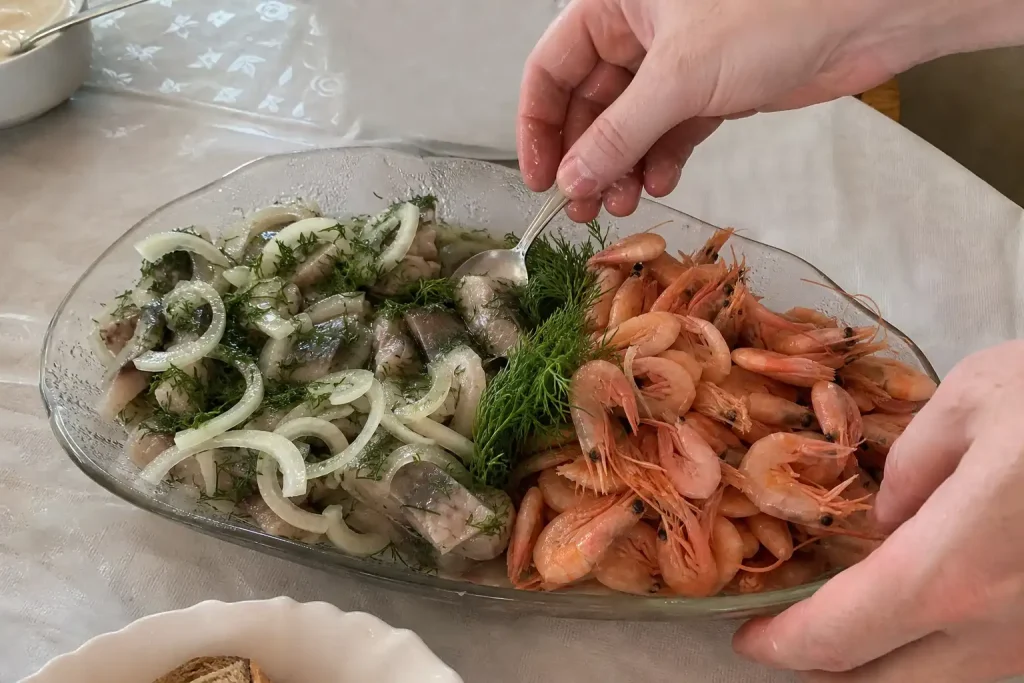 Händer justerar ett fat med inlagd sill och räkor på midsommarbordet, till artikeln om så länge kan midsommarmaten stå framme