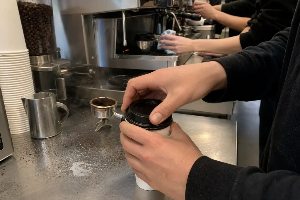 Barista sätter lock på pappersmugg vid kaffebar, i samband med att Starbucks varslar personal.
