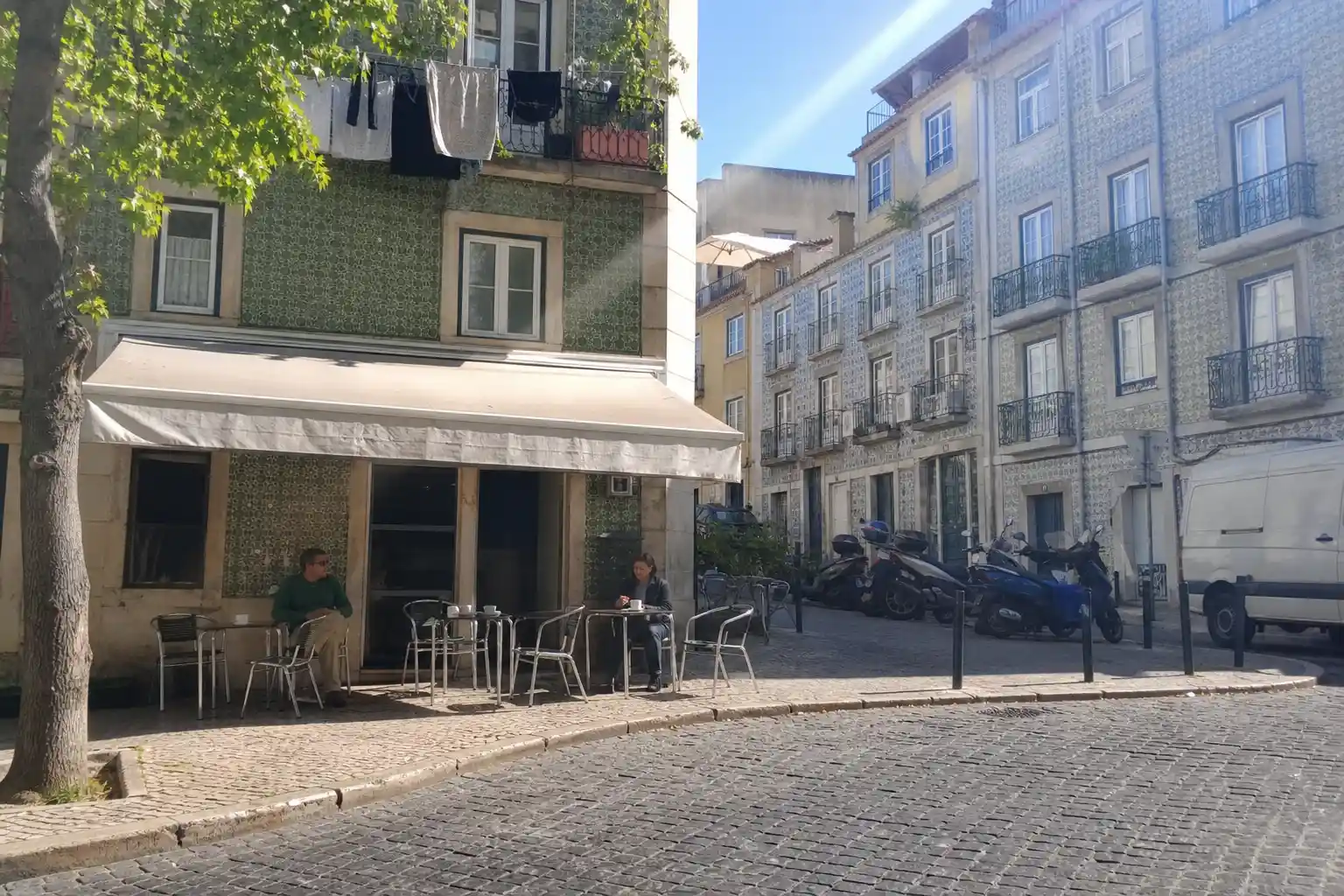 Litet gathörnskafé i Lisboa med bord utomhus, en vardaglig scen som fångar känslan av att dricka kaffe i Portugal.