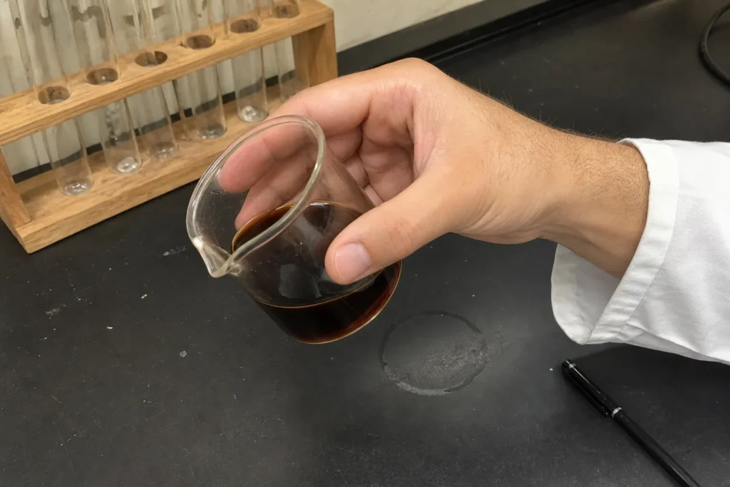 Hand lutar en bägare med mörk vätska på labbänk, kopplat till att koffein kan flippa en åldringsrelaterad cellswitch