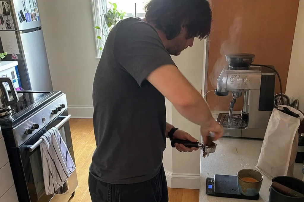En person tampar koffeinfritt kaffe i en portafilter vid en espressomaskin i köket en vardaglig morgon.